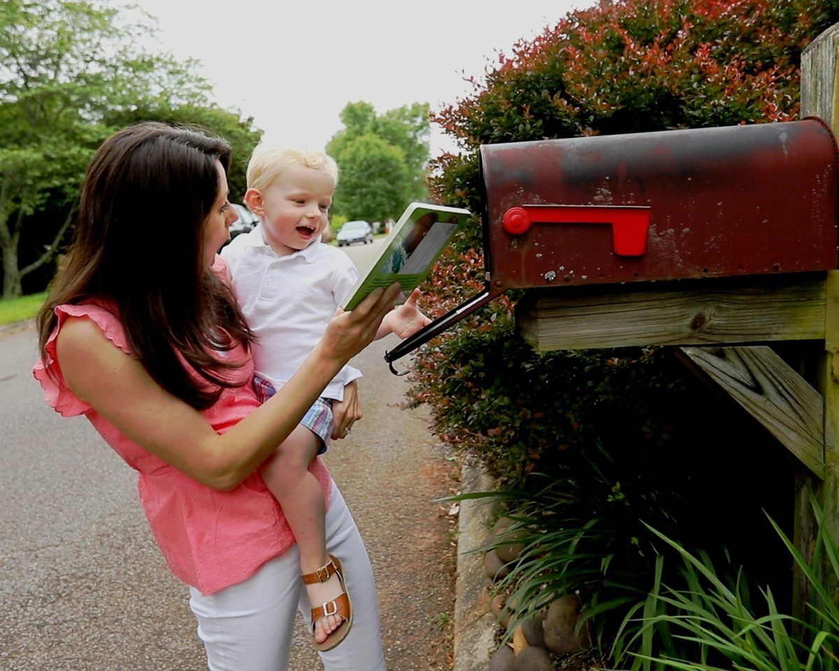 A parent and toddler taking a book out of the mailbox